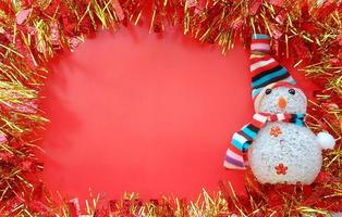 decorazioni natalizie lucide rosse e dorate e pupazzo di neve con cappello a righe e sciarpa su sfondo rosso. biglietto di auguri di natale. cornice del bordo orizzontale con spazio per la copia del testo foto