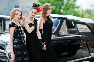 tre giovani ragazze in abito stile retrò vicino a vecchie auto d'epoca classiche. foto