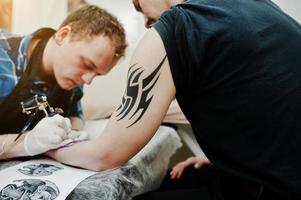 il maestro del tatuaggio fa un tatuaggio per l'uomo rocker al salone di tatuaggi foto