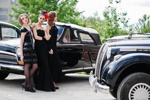 tre giovani ragazze in abito stile retrò vicino a vecchie auto d'epoca classiche. foto