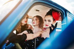 tre giovani ragazze in abito stile retrò sede su una vecchia auto d'epoca classica. foto