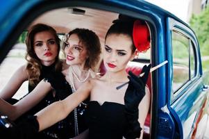 tre giovani ragazze in abito stile retrò sede su una vecchia auto d'epoca classica. foto