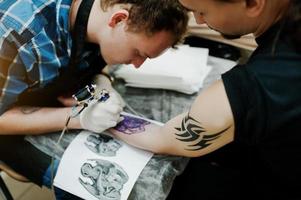 il maestro del tatuaggio fa un tatuaggio per l'uomo rocker al salone di tatuaggi foto