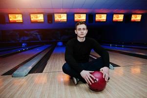 giovane in possesso di una palla da bowling seduto contro piste da bowling con luce ultravioletta. foto