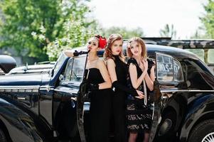 tre giovani ragazze in abito stile retrò vicino a vecchie auto d'epoca classiche. foto