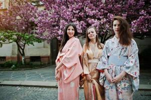 tre ragazze europee che indossano il tradizionale kimono giapponese sfondo albero di sakura rosa fiorito foto