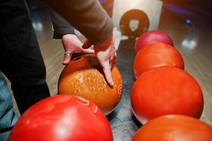 primo piano della mano del giocatore di bowling che prende la palla arancione dall'ascensore della ciotola foto