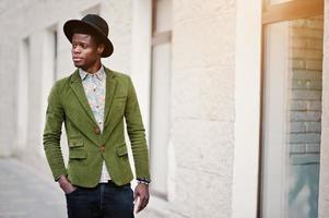 primo piano ritratto di moda di uomo afroamericano nero su giacca di velluto verde e cappello nero che cammina per le strade dello sfondo della città casa con molte finestre foto