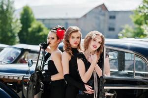 tre giovani ragazze in abito stile retrò vicino a vecchie auto d'epoca classiche. foto