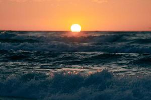 mezzo sole sotto l'orizzonte sulle onde del mare blu, bellissimo tramonto sul mare, paesaggio marino mozzafiato foto