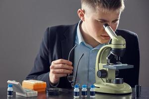 il ragazzo osserva la droga attraverso un microscopio. primo piano sul ricercatore che lavora con il microscopio in laboratorio foto