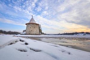 antica pskov in inverno. la torre piatta del Cremlino di pskov contro il cielo blu. in primo piano, il fiume è coperto di ghiaccio. foto