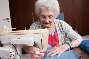 signora anziana a casa che lavora alla sua macchina da cucire foto