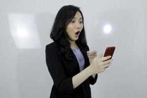 la giovane ragazza asiatica di affari è shock e felice nello smartphone sullo sfondo bianco isolato foto
