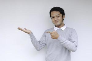 il giovane uomo asiatico è sorridente e felice con il punto della mano sullo spazio vuoto foto