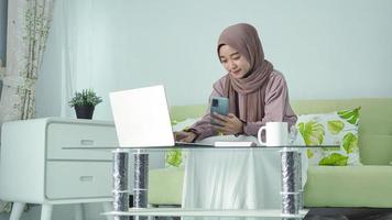 donna asiatica in hijab che lavora da casa in cerca di idee sullo schermo del suo smartphone foto