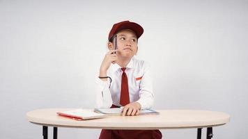 ragazza asiatica della scuola elementare che pensa a un'idea da scrivere isolata su un fondo bianco foto