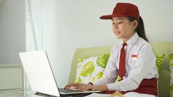 ragazza asiatica della scuola elementare che studia online da casa digitando sul computer portatile foto