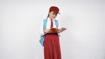 ragazza asiatica della scuola elementare che legge un libro felicemente isolato su fondo bianco foto