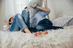 le giovani coppie in jeans si divertono a combattere su un letto foto
