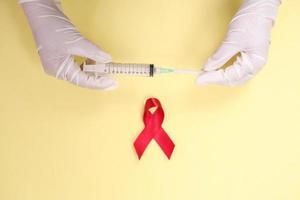 nastro rosso con guanti medici e siringa contro l'hiv isolato su sfondo giallo foto