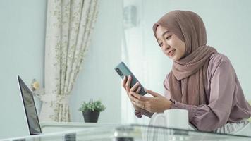 donna asiatica in hijab che guarda lo schermo del telefono felicemente a casa foto