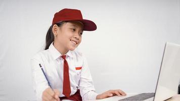 ragazza asiatica della scuola elementare che scrive idea dallo schermo del computer portatile isolato su priorità bassa bianca foto