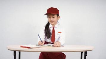 ragazza asiatica della scuola elementare che impara a scrivere isolata su fondo bianco foto
