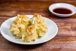 gnocco cinese al vapore, shumai su piatto bianco servito con salsa di soia su tavola di legno. delizioso maiale dimsum. foto