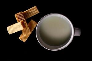 vista dall'alto quattro wafer in un piatto bianco con una tazza di latte su sfondo nero con spazio per la copia. foto