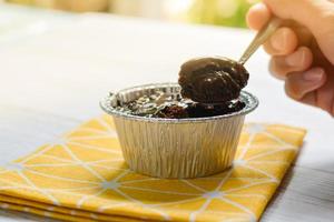 mangiare una torta al cioccolato fondente con guarnizione di gocce di cioccolato in una tazza di alluminio con un cucchiaio di metallo su una tovaglia gialla. deliziosa pasticceria dolce in caffetteria. copia spazio per il tuo testo. foto