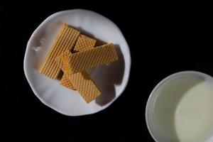 vista dall'alto quattro wafer in un piatto bianco con una tazza di latte su sfondo nero con spazio per la copia. foto