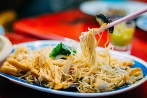 delizioso cibo cinese. mangiare noodle saltati in padella e shiitake con le bacchette servono nel ristorante della città cinese in tailandia. messa a fuoco selettiva. foto