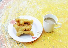 primo piano di patongko stick di pasta fritta e tazza di caffè bianca sul tavolo con sopra foto