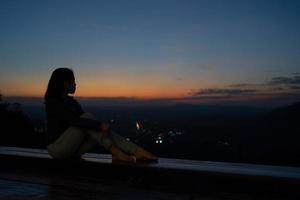 silhouette di donna seduta sulla terrazza e guardando il tramonto sulla montagna foto