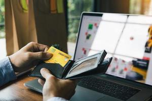 la mano asiatica dell'uomo sta tirando fuori una carta di credito dalla tasca per completare lo shopping online sul computer. foto