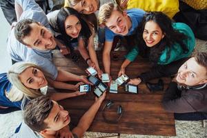 vista dall'alto cerchio delle mani usando il telefono nella caffetteria - amici multirazziali scena interna dipendente da dispositivi mobili dall'alto - persone connesse wifi nella riunione del tavolo del bar - concetto di lavoro di squadra foto