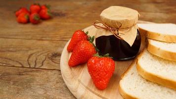 fette di pane e delizioso vasetto di marmellata di fragole e frutti di bosco freschi su legno foto