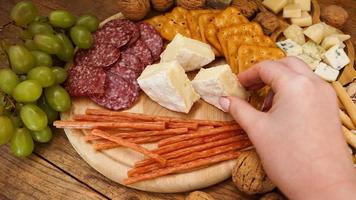 una mano di donna prende un pezzo di camembert da un piatto di formaggi foto