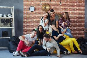 ritratto di gruppo di ragazzi e ragazze multietnici con abiti colorati alla moda che tengono un amico in posa su un muro di mattoni, persone in stile urbano che si divertono, concetti sullo stile di vita insieme giovanile foto