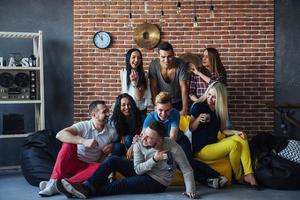 ritratto di gruppo di ragazzi e ragazze multietnici con abiti colorati alla moda che tengono un amico in posa su un muro di mattoni, persone in stile urbano che si divertono, concetti sullo stile di vita insieme giovanile foto