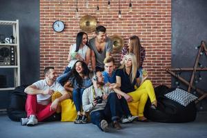 ritratto di gruppo di ragazzi e ragazze multietnici con abiti colorati alla moda che tengono un amico in posa su un muro di mattoni, persone in stile urbano che si divertono, concetti sullo stile di vita insieme giovanile foto