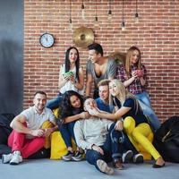 ritratto di gruppo di ragazzi e ragazze multietnici con abiti colorati alla moda che tengono un amico in posa su un muro di mattoni, persone in stile urbano che si divertono, concetti sullo stile di vita insieme giovanile foto