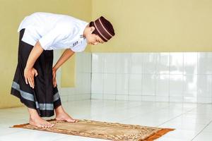 giovane uomo musulmano asiatico che fa salat con gesto ruku sul tappeto da preghiera foto