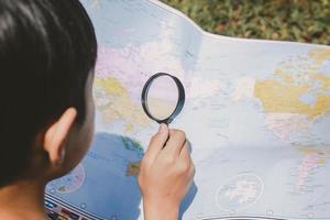 un ragazzo che cerca la posizione sulla mappa del mondo usando la lente d'ingrandimento foto