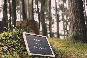 albero abbattuto e citazione sulla lavagna dice salva il nostro pianeta sdraiato sull'erba verde della foresta foto