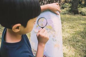 un ragazzo che cerca la posizione sulla mappa del mondo usando la lente d'ingrandimento foto