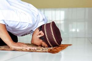 primo piano di un uomo religioso musulmano che fa salat con posa di prostrazione sul tappeto da preghiera foto