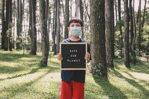 un ragazzo che mostra una citazione sulla lavagna dice di salvare il nostro pianeta con la foresta sullo sfondo, concetto di giorno della terra foto