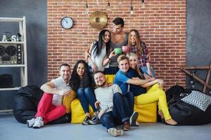 ritratto di gruppo di ragazzi e ragazze multietnici con abiti colorati alla moda che tengono un amico in posa su un muro di mattoni, persone in stile urbano che si divertono, concetti sullo stile di vita insieme giovanile foto